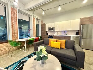 Un salon moderne avec un canapé gris, une table basse agrémentée d’une plante et un coin repas avec des chaises vertes.