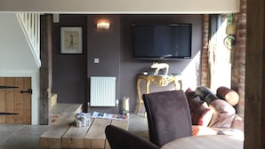 A cozy living room with a wooden table, comfortable seating, a fireplace, and a television mounted on the wall. - Impeccable Cottage Suitable for 2 Adults & 1 Child (York)