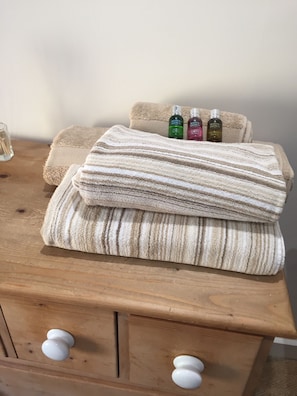 A wooden chest with a folded beige and white striped towel, a beige towel, and three bottles of Molton Brown body lotion.