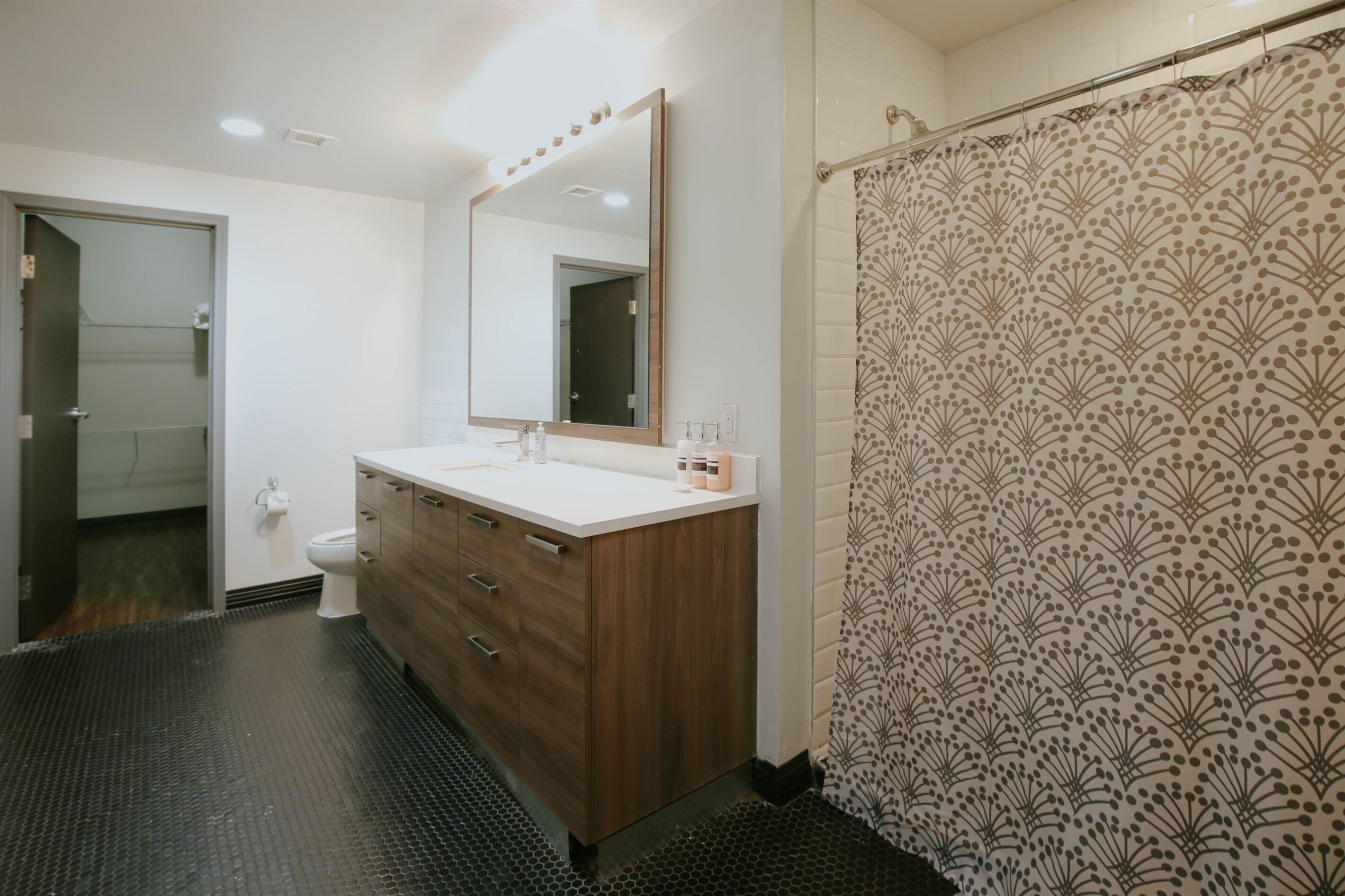 Un baño con tocador de madera, un espejo grande, inodoro y cortina de ducha con estampado floral.