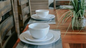 Un comedor con una mesa de madera dispuesta para dos personas, un microondas y una planta en maceta.
