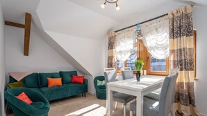 Een moderne woonkamer met een groene bank, een eettafel en een raam met gordijnen.