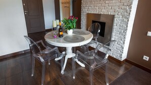Een eetgedeelte met een ronde tafel, transparante stoelen, een bloevas en een bakstenen muur.