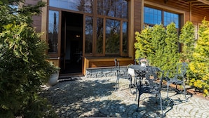Een houten huis met een stenen terras, een tafel en stoelen.