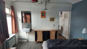 Un dormitorio con una cama, una silla de madera, un escritorio con lavamanos y un espejo.