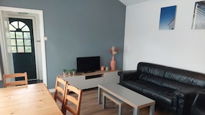 Una sala de estar con una mesa de comedor de madera, un sofá de cuero negro, un televisor sobre un mueble de madera y un banco.