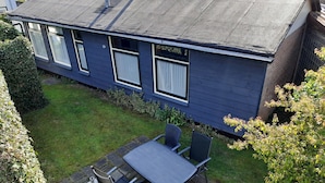 Un patio con una mesa y sillas, un pequeño jardín y un edificio con ventanas.