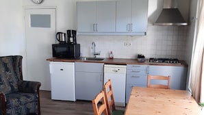 Cocina compacta con armarios blancos, una mesa de comedor de madera y una cafetera.