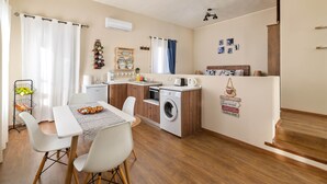 Cocina compacta con lavadora, una mesa de comedor con sillas y un refrigerador pequeño.