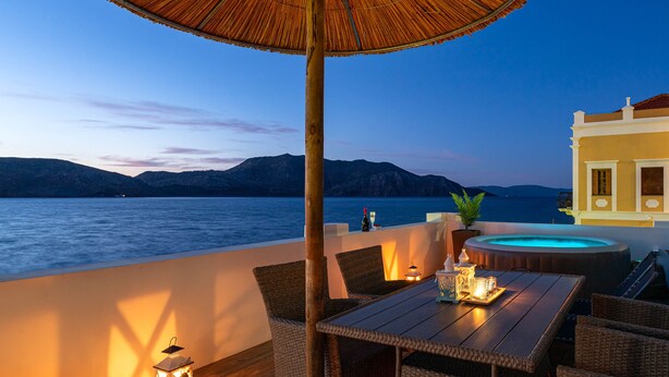 Una terraza de madera con mobiliario de mimbre, una mesa con velas, un farol y un jacuzzi.
