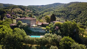 A traditional stone building with a swimming pool surrounded by lush greenery and hills in the background.