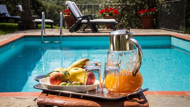 A poolside breakfast setup with fruits, a pitcher of orange juice, and a teapot.