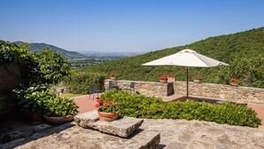 An outdoor patio with stone walls, potted plants, and a white umbrella.