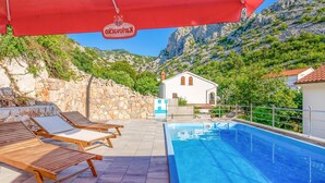 Zona de piscina con sillas de descanso, una piscina e imponentes montañas al fondo.