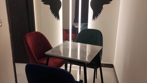 Una habitación pequeña y moderna con una mesa cuadrada y tres sillas en rojo, azul y verde azulado.