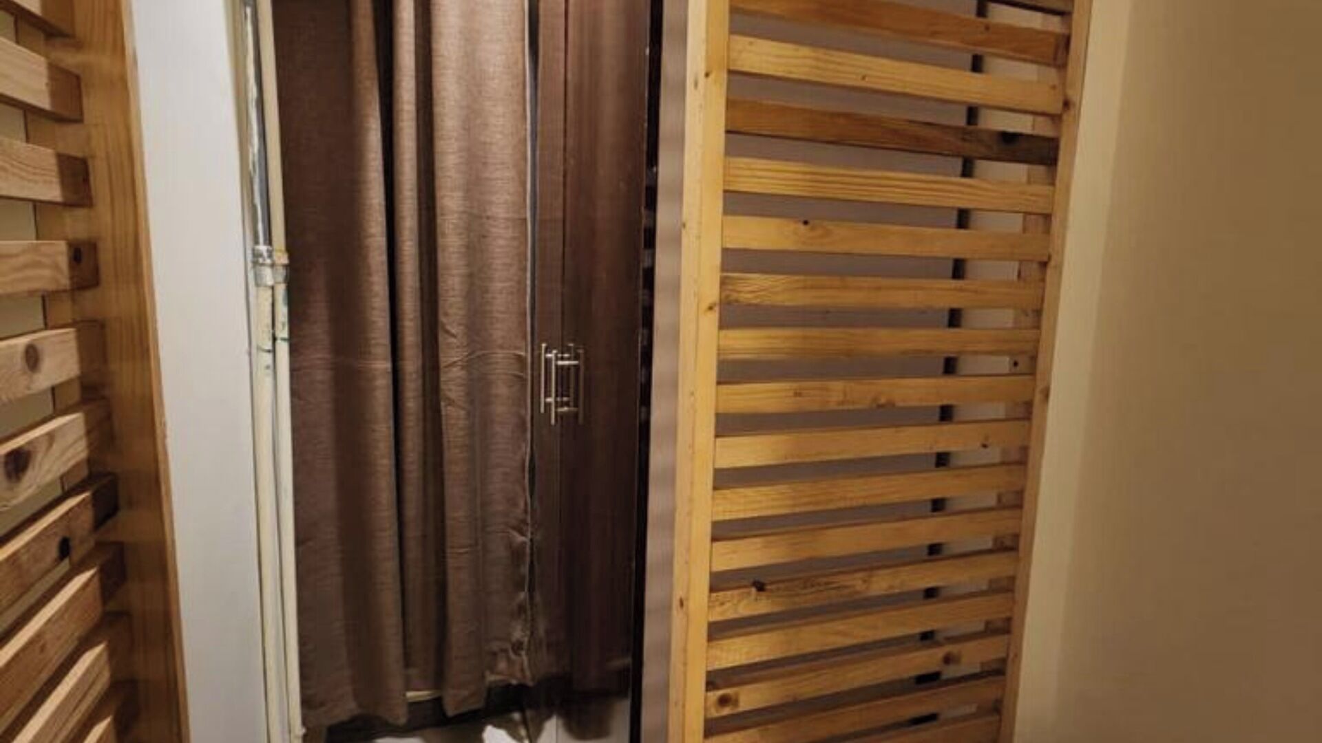 Une porte en bois dotée d’un système coulissant, un rideau et un mur recouvert de panneaux en bois.