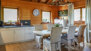 A wooden cabin interior with a dining table, wicker chairs, a kitchen with a clock, and a painting on the wall. - Stunning home in Nimsreuland with WiFi (Nimsreuland)