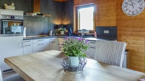 A kitchen with wooden walls, a large window, a clock, and a dining table with a potted plant. - Stunning home in Nimsreuland with WiFi (Nimsreuland)
