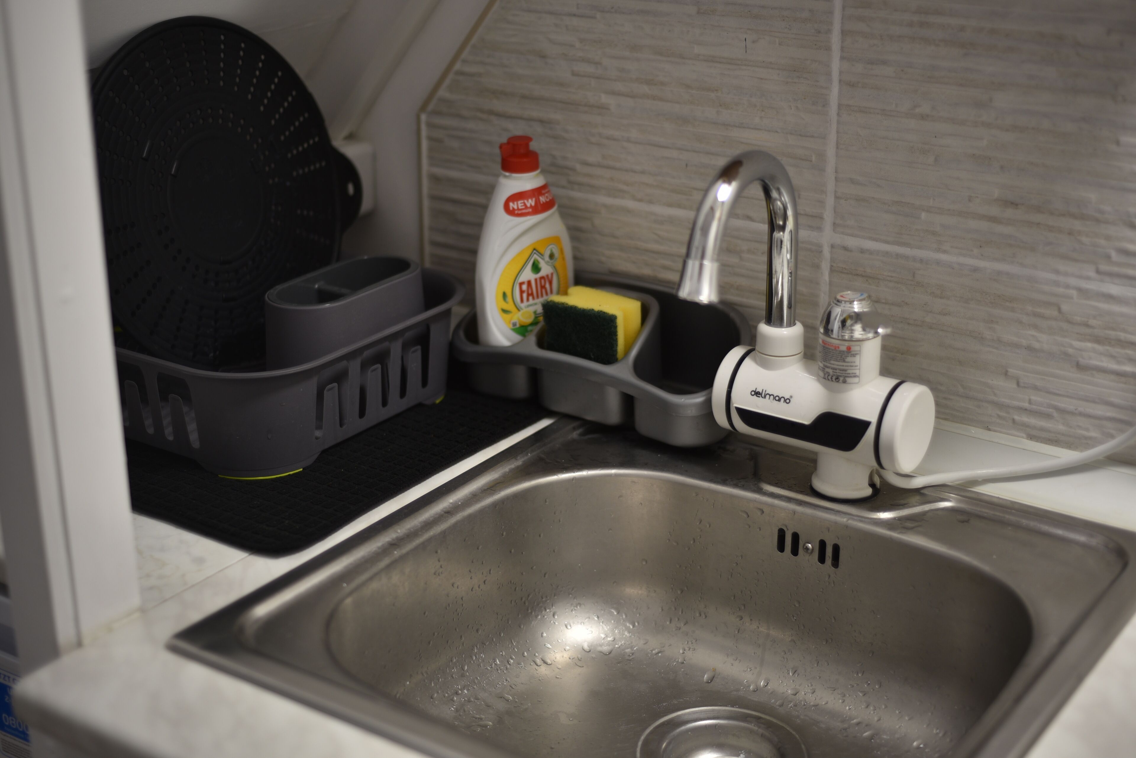 A kitchen sink with a dish rack, a bottle of Fairy dish soap, a sponge, and a dehumidifier.