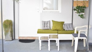Een witte deur met een raam erboven, een groene bank met kussens, en twee witte stoelen.