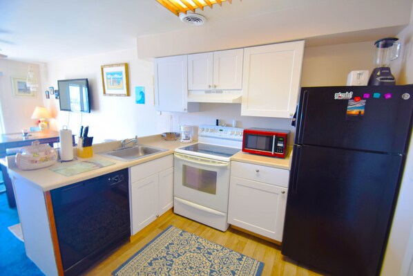 A compact kitchen with white cabinetry, a black refrigerator, a microwave, and a stove.