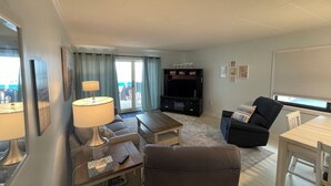 A living room with a sofa, armchair, TV stand, and a dining table. - Ocean Hideaway 111-Oceanfront 18th St, Free WiFi, Elev, W/D, AC (Ocean City)