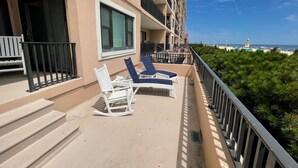 A balcony with two white rocking chairs and a table, overlooking a beach with a lighthouse in the distance. - Ocean Hideaway 111-Oceanfront 18th St, Free WiFi, Elev, W/D, AC (Ocean City)