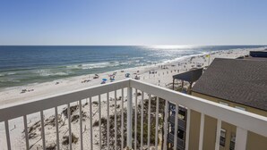 A beach view from a balcony overlooking a sandy beach with umbrellas and beachgoers. - Dog friendly beachfront condo with sunset view (Gulf Shores)