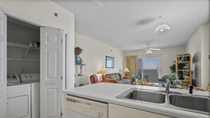 A modern kitchen with a built-in dishwasher, a double sink, and a dining area with a sofa and table. - Dog friendly beachfront condo with sunset view (Gulf Shores)