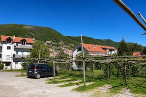 A rural setting with a parked car, a vineyard, and houses with red-tiled roofs.