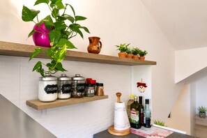 Una cocina con estantes que contienen frascos etiquetados como 'ZUCCHERO', 'SALE' y 'COFEE', un rodillo de madera y una botella de aceite de oliva virgen extra.