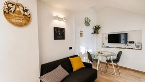 A modern living room with a dark sofa, a round glass table, and a TV mounted on the wall. - Raffaella Holiday Home, Agerola & Amalfi Coast (Agerola)