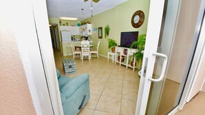 A living room with a blue sofa, a dining area with a table and chairs, and a kitchen in the background. - Dog friendly beachfront condo with in/out pools (Gulf Shores)