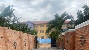 A courtyard with a gravel ground, brick walls, and a blue building in the background. - Cosy Rooms Away in a Stunning House (Koforidua)