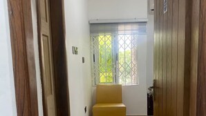 A hallway with a yellow bench, wooden doors, and a window with a view of greenery. - Cosy Rooms Away in a Stunning House (Koforidua)