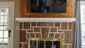 Una sala de estar con chimenea de piedra, un televisor de pantalla plana montado encima y un ventilador de techo.