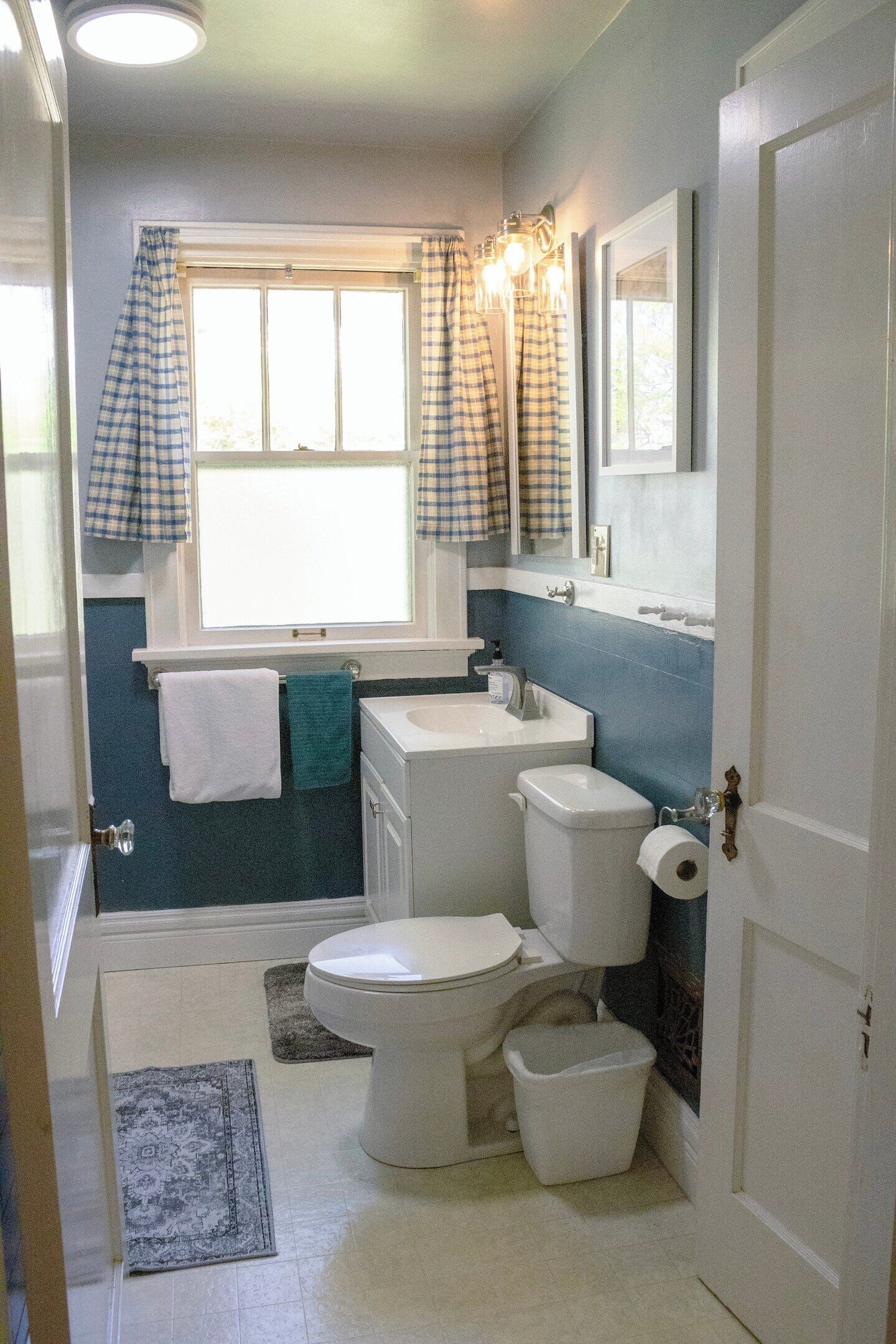 Une salle de bain avec des toilettes, un lavabo et une fenêtre avec des rideaux.