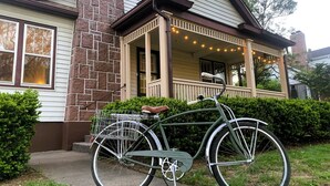 Una bicicleta verde con canasta y asiento marrón estacionada frente a una casa con porche.