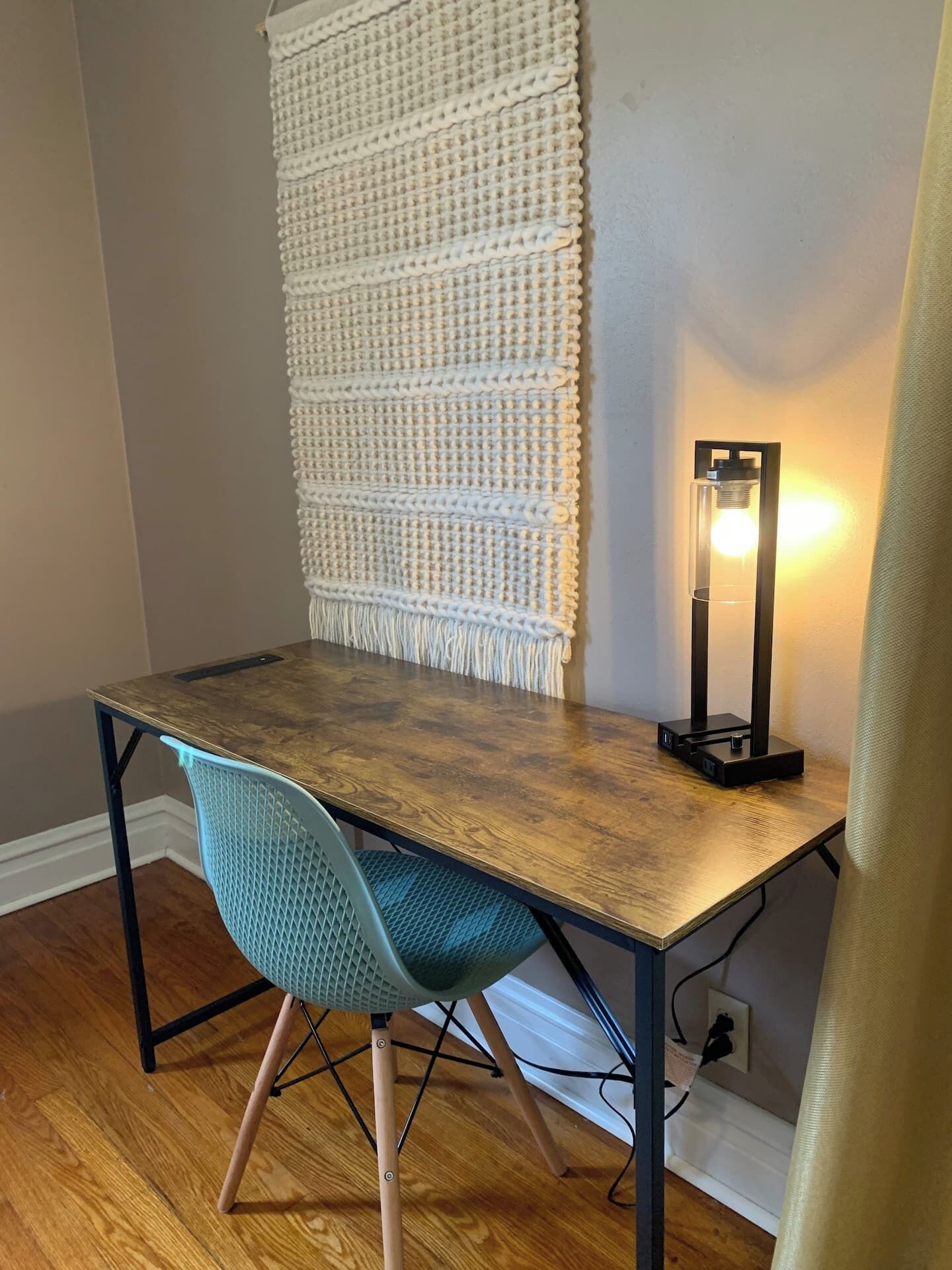 A wooden desk with a macrame wall hanging, a modern chair, and a floor lamp.