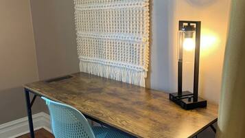 A wooden desk with a macrame wall hanging, a modern chair, and a floor lamp.