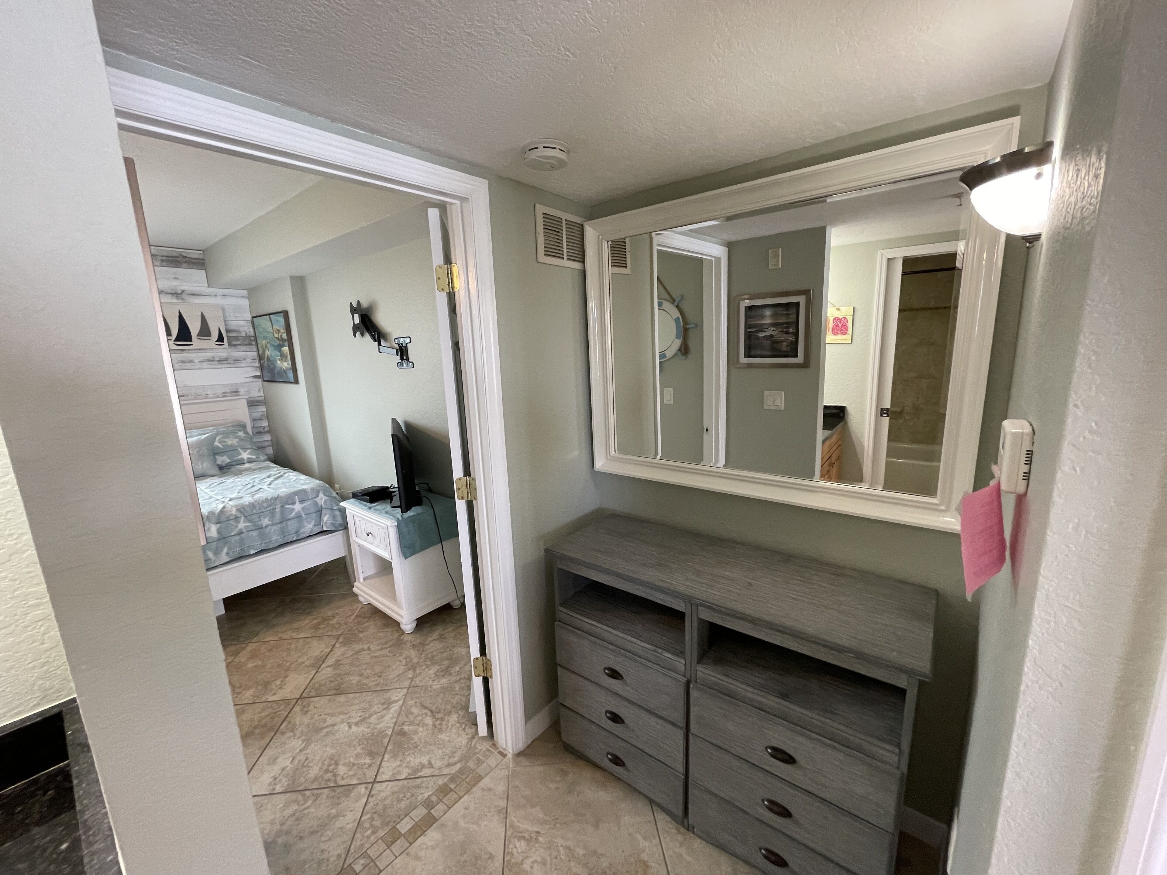 A bedroom with a bed, a dresser, a mirror, and a door leading to another room.
