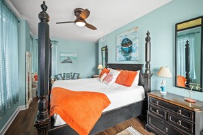 Un dormitorio con cama, mesitas de noche, cómoda, ventilador de techo y obras de arte en las paredes.