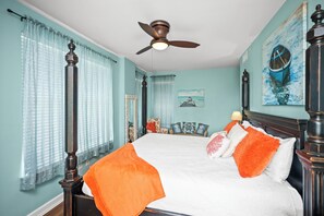 Ein Schlafzimmer mit einem Bett, Vorhängen, einem Deckenventilator und Kunstwerken an den Wänden.