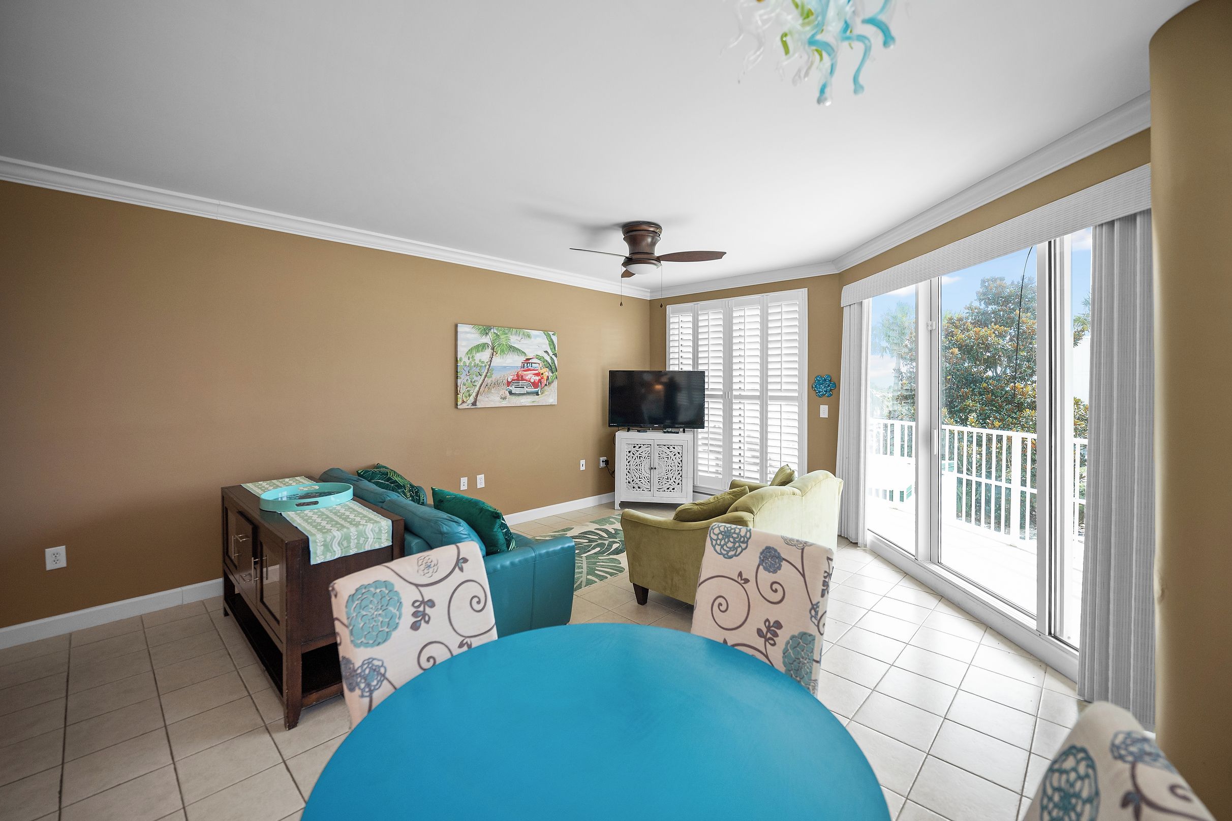 A living room with a ceiling fan, a flat-screen TV, and a large window with a view of the outdoors.