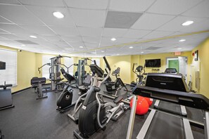 A gym with various exercise machines, a treadmill, and a red exercise ball.
