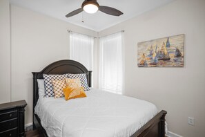 A bedroom with a bed, a nightstand, a ceiling fan, and a painting on the wall.