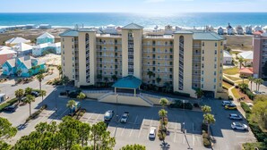 A multi-story hotel with a central courtyard, parking lot, and a view of the ocean.
