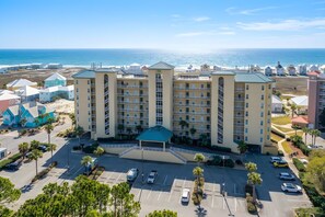 A multi-story hotel with a central courtyard, parking lot, and a view of the ocean.