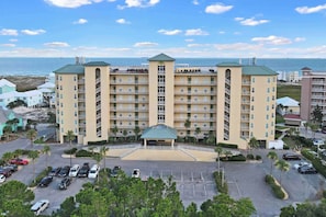 A multi-story hotel with a central courtyard, parking lot, and a view of the ocean. - Stunning 3BR Gulf-View Condo Ground-Floor (Gulf Shores)