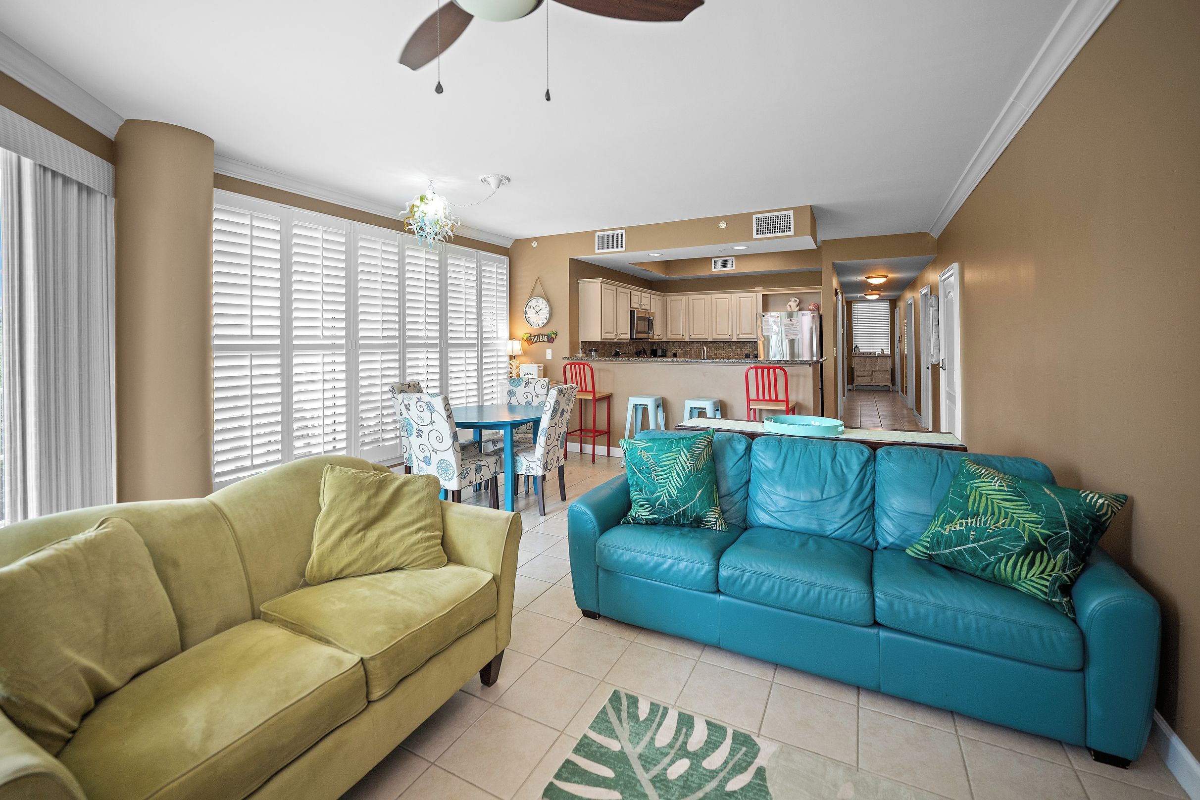 A living room with a yellow sofa, a blue sofa with green cushions, and a dining area with patterned chairs.